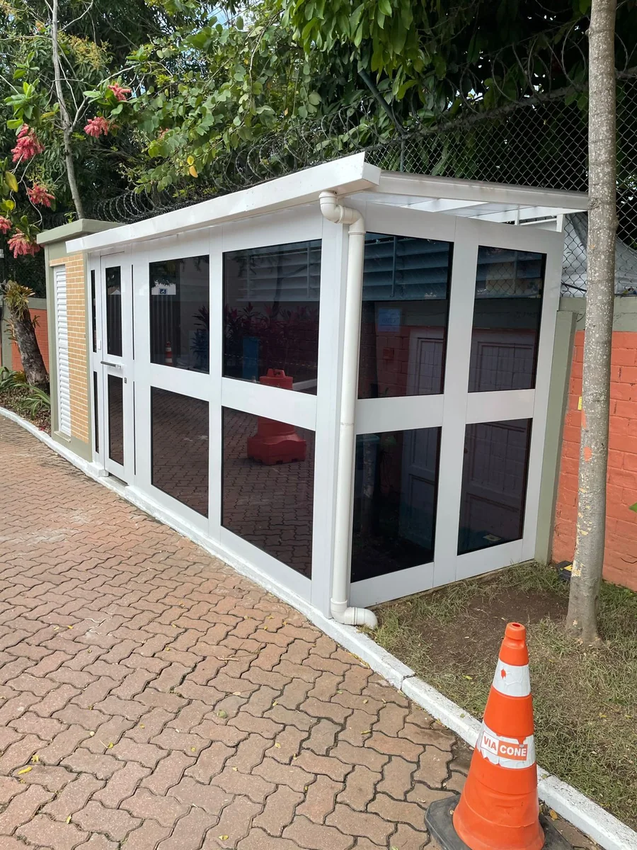 Guarita branca com painéis envidraçados instalada em área externa pavimentada; projeto real do grupo.