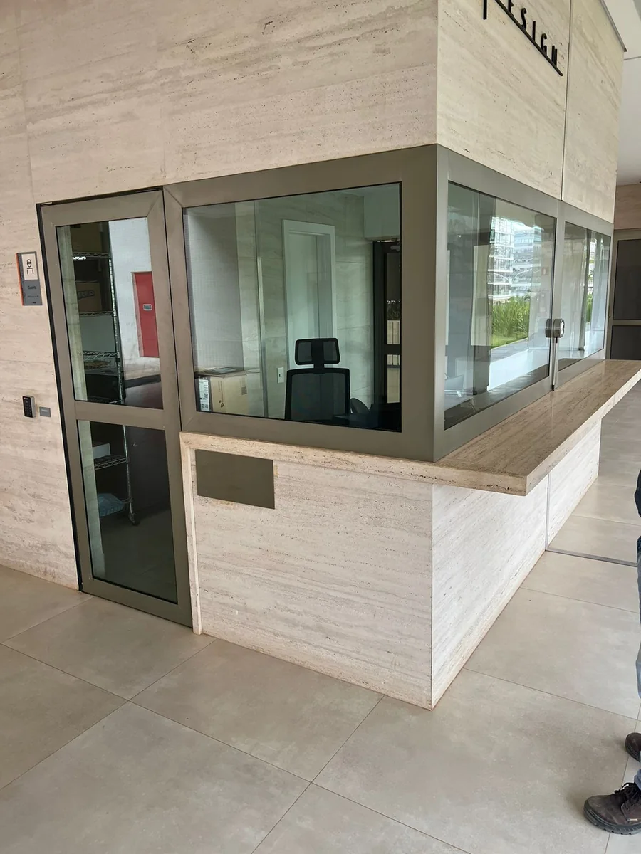 Portaria com porta de vidro, janela de atendimento e revestimento claro em pedra; projeto real do grupo.